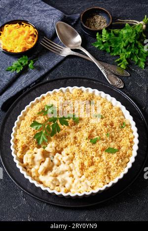 mac cuit au four et fromage saupoudré de chapelure panko et de persil frais dans un plat allant au four sur une table en béton avec fourchette et cuillère, vue verticale Banque D'Images