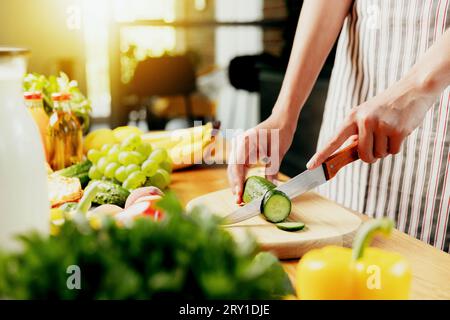 Gros plan sur la femme au foyer, la fille coupe le concombre à la cuisine sur la planche à découper. Femme faisant de la salade saine à faible teneur en calories, préparer des detox verts Banque D'Images
