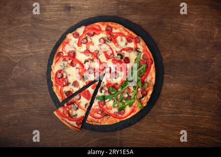 Pizza avec saucisses fumées, fromage, champignons, tomates cerises, poivrons et légumes verts sur une pierre et une planche en bois brun, vue de dessus. Banque D'Images