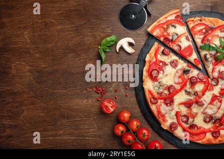 Pizza avec saucisses fumées, fromage, champignons, tomates cerises, poivrons et légumes verts sur une pierre et une planche en bois brun, vue de dessus. Banque D'Images