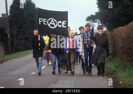 Jeunes anarchistes manifestants de la paix marchent d'Aldermaston à Greenham Common vendredi Saint Pâques 1983. Les manifestants pour la paix (pas ce groupe) formaient une chaîne humaine qui s'étendait sur 14 milles. Ils ont tracé une route le long de ce que les manifestants appellent la "Nuclear Valley" dans le Berkshire. La chaîne a commencé à la base aérienne américaine de Greenham Common, a dépassé le centre de recherche nucléaire d'Aldermaston et s'est terminée à l'usine de munitions de Burghfield. Un jeune anarchiste fait un geste de la main au Salut de la paix. ANNÉES 1980 ROYAUME-UNI HOMER SYKES Banque D'Images