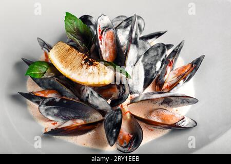 Moules de fruits de mer en sauce crème avec citron et basilic dans une assiette blanche. Vue de dessus . Banque D'Images