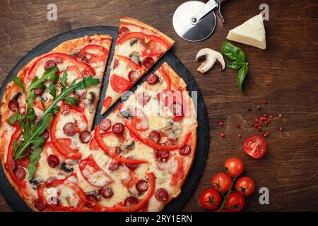 Pizza avec saucisses fumées, fromage, champignons, tomates cerises, poivrons et légumes verts sur une pierre et une planche en bois brun, vue de dessus. Banque D'Images