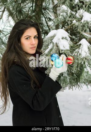 Jeune fille brune décore un sapin avec des jouets en plein air Banque D'Images