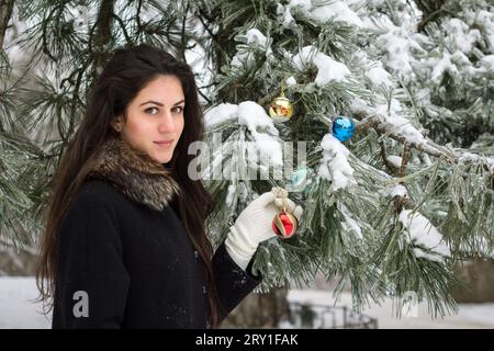 Atractive Beauty girl décore un sapin avec des jouets en plein air Banque D'Images