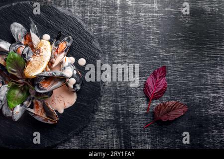 Moules de fruits de mer en sauce crème avec citron et basilic sur une pierre et un tableau noir. Vue de dessus avec espace pour votre texte. Banque D'Images