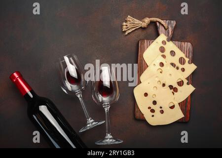 Bouteille de vin, deux verres et fromage maasdam tranché sur une planche à découper sur fond rouillé. Vue de dessus. Banque D'Images