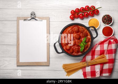 Boulettes de viande en sauce tomate avec épices et basilic dans une poêle et tomates cerises sur une planche de bois blanche. Vue de dessus avec espace pour votre texte. Banque D'Images