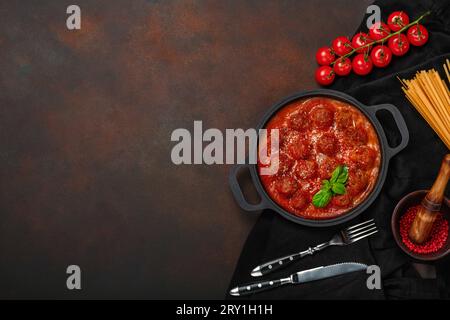 Boulettes de viande en sauce tomate avec épices, tomates cerises, pâtes et basilic dans une poêle sur fond brun rouillé. Vue de dessus avec espace pour votre texte. Banque D'Images