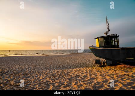 Coucher de soleil sur la plage sur la mer Baltique polonaise. Bateau de pêche dans la soirée près de Międzyzdroje, Pologne. Banque D'Images