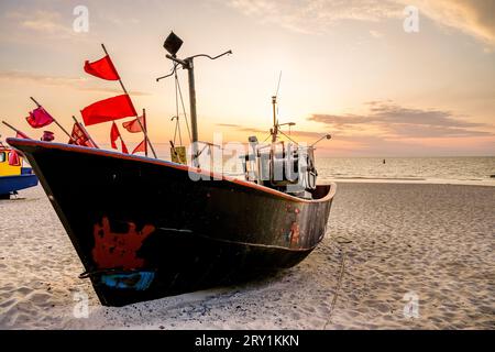 Coucher de soleil sur la plage sur la mer Baltique polonaise. Bateau de pêche dans la soirée près de Międzyzdroje, Pologne. Banque D'Images