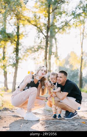 Heureux jeunes parents s'amusent et soufflent des bulles de savon avec son tout-petit garçon dans le parc. Banque D'Images