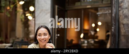 Portrait d'une fille asiatique travaille à l'extérieur dans un café, s'assoit avec un ordinateur portable, des études, sourires heureux Banque D'Images