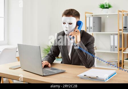 Homme anonyme en masque facial fait des appels téléphoniques pour arnaquer les gens et voler leur argent Banque D'Images