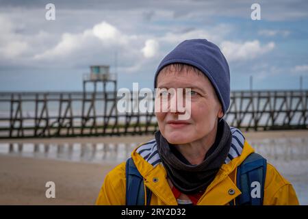 Portrait d'une femme mûre aux yeux bleus debout devant le Fisherman's Pier en bois, portant une cire jaune, un t-shirt rayé, une casquette de marin bleue Banque D'Images