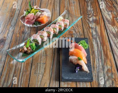 D'en haut de délicieux sushi uramaki et nigiri sushi avec sashimi dans de petits bols sur fond en bois Banque D'Images