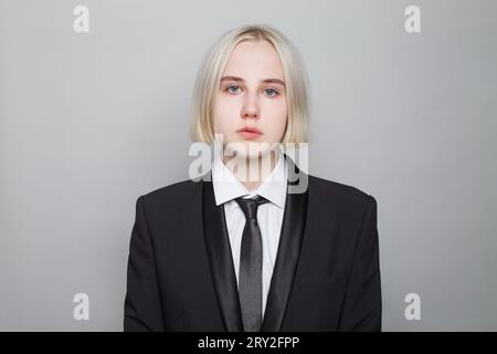 Parfaite jeune femme d'affaires adulte avec coupe de cheveux blonde droite courte portant costume de style masculin noir avec cravate Banque D'Images