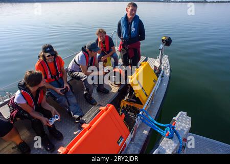 28 septembre 2023, Saxe-Anhalt, Arendsee : Sven Thomas (à droite), archéologue sous-marin de l'Office d'État de Saxe-Anhalt pour la préservation des monuments et de l'archéologie, se tient sur le lac Arendsee à bord d'un bateau THW à côté de ses collègues et surveille plusieurs moniteurs. Les archéologues enquêtent sur des sites au fond du lac Arendsee depuis le 25 septembre 2023. Au total, 20 cibles seront étudiées en haute résolution et en 3D d’ici la fin de la semaine. Entre autres choses, des clôtures à poissons de différentes époques ont été découvertes. L'Institut Fraunhofer d'Optronique, d'Ingénierie des systèmes et d'IMA Banque D'Images