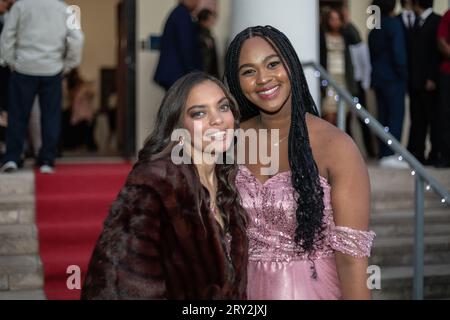 Dans un gros plan au bal, deux amis multiraciaux se tiennent en toute confiance sur un escalier recouvert de moquette rouge, rayonnant d'élégance et de camaraderie. Banque D'Images