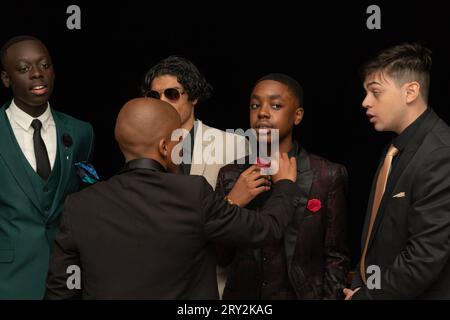 Dans une capture en gros plan, cinq jeunes hommes multiraciaux au bal de promo s'engagent dans une conversation animée tandis que l'un ajuste habilement le noeud papillon de l'autre Banque D'Images