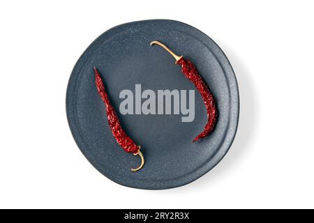 Assiette en céramique grise vide avec des piments forts séchés isolés sur fond blanc. Vue de dessus avec espace de copie. Banque D'Images