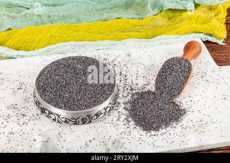 Graines de pavot. Plat de graines de pavot avec peluche foncée dans la louche en bois ou cuillère isolé sur fond de marbre. Petit-déjeuner vitaminé snack, régime alimentaire et alimentation saine Banque D'Images