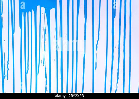 La peinture coule sur une surface bleu clair. Un arrière-plan avec des bandes de couleur. Flux verticaux de peinture. Structure abstraite de fond Banque D'Images