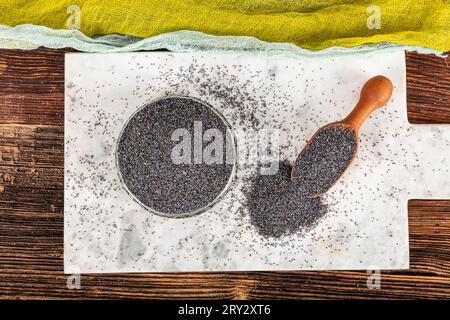 Graines de pavot. Plat de graines de pavot avec peluche foncée dans la louche en bois ou cuillère isolé sur fond de marbre. Petit-déjeuner vitaminé snack, régime alimentaire et alimentation saine Banque D'Images