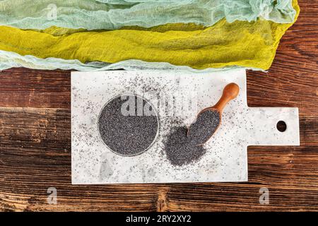 Graines de pavot. Plat de graines de pavot avec peluche foncée dans la louche en bois ou cuillère isolé sur fond de marbre. Petit-déjeuner vitaminé snack, régime alimentaire et alimentation saine Banque D'Images