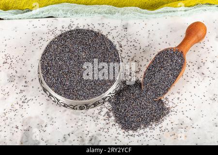 Graines de pavot. Plat de graines de pavot avec peluche foncée dans la louche en bois ou cuillère isolé sur fond de marbre. Petit-déjeuner vitaminé snack, régime alimentaire et alimentation saine Banque D'Images