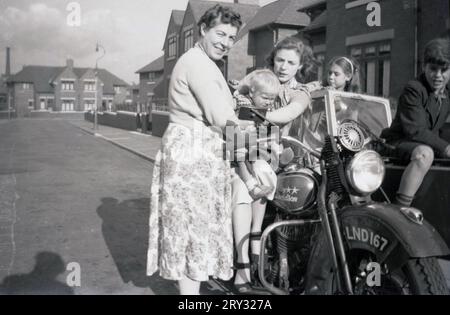 Années 1950, historique, dehors dans une rue de banlieue, deux mères avec des enfants tbeir se sont rassemblées à côté et sur une moto Harley Davidson et sidecar de l'époque, Oldham, Angleterre, Royaume-Uni. Banque D'Images