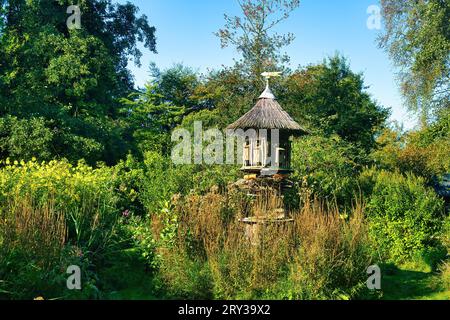 Grande structure en bois un chaume dans un jardin arboré, avec nichoirs pour les oiseaux et un hôtel à insectes Banque D'Images