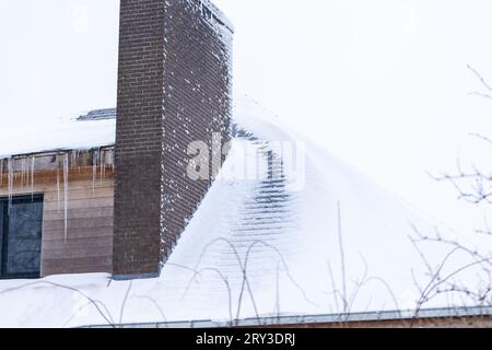 Portrait d'un toit d'une maison pleine de neige blanche, à l'exception d'un sentier qui a fondu à cause d'un mauvais isolement. Il y a une grande cheminée en brique et le toit aller Banque D'Images