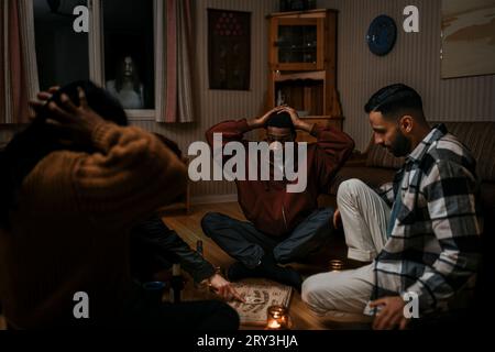 Amis choqués regardant la femme toucher le tableau de ouija tandis que fantôme à la fenêtre dans la cabane en rondins Banque D'Images