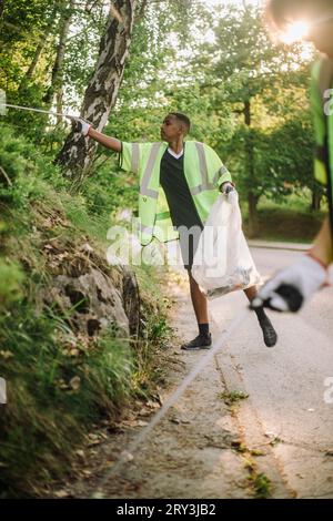 Adolescent portant des vêtements réfléchissants ramassant du plastique par les plantes Banque D'Images