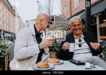 Heureux amis seniors masculins appréciant les uns avec les autres tout en prenant un café au café Sidewalk Banque D'Images