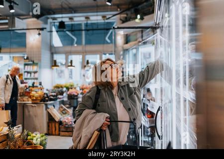 Femme âgée atteignant pour le produit tout en faisant l'épicerie dans le supermarché Banque D'Images