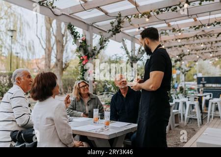 Des amis seniors masculins et féminins donnant de la nourriture à un serveur debout au restaurant Banque D'Images