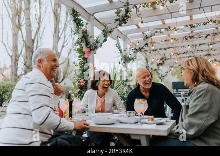 Joyeux amis seniors masculins et féminins riant tout en prenant de la nourriture au restaurant Banque D'Images