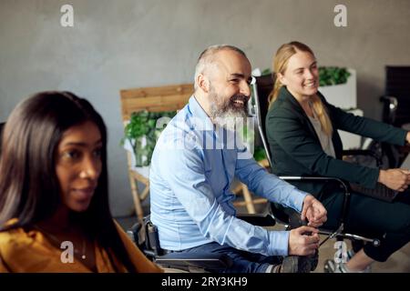 Heureux homme d'affaires barbu avec handicap assis au milieu de collègues féminines dans le bureau créatif Banque D'Images