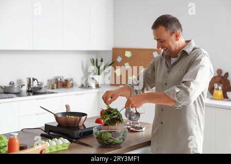 Homme mûr faisant salade de légumes dans la cuisine Banque D'Images