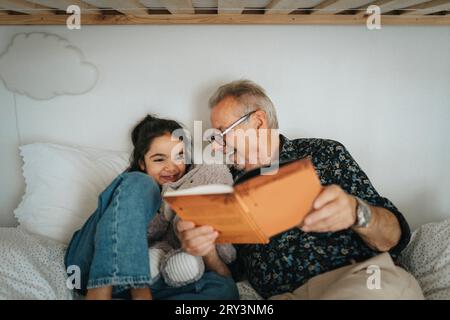 Heureux homme senior lisant livre de contes avec petite-fille sur le lit à la maison Banque D'Images