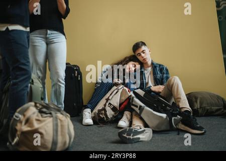 Frère et sœur prenant le repos tout en étant assis au milieu des bagages près du mur jaune Banque D'Images