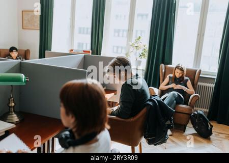 Adolescent assis près des étudiantes dans la bibliothèque Banque D'Images