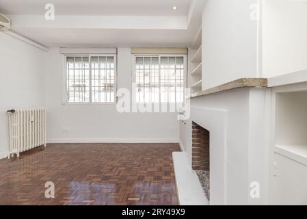 Salon dans l'appartement avec cheminée intégrée, barres métalliques sur les fenêtres et étagères en bois blanc assorties Banque D'Images