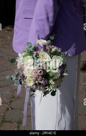 Gros plan de mariée moderne tenant un bouquet de mariage avec des fleurs blanches et violettes Banque D'Images