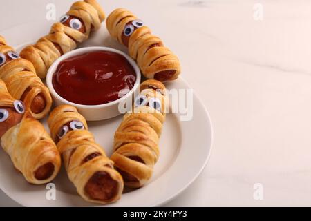 Assiette avec de savoureuses momies de saucisse pour la fête d'Halloween et ketchup sur la table blanche, closeup. Espace pour le texte Banque D'Images