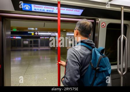 Homme debout près de la porte ouverte de la liaison ferroviaire de l'aéroport. Le tableau au néon au-dessus avec des messages en anglais et chinois - fermeture des portes, s'il vous plaît debout cle Banque D'Images