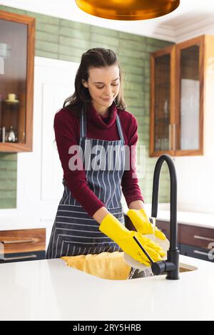 Heureuse femme caucasienne portant un tablier faisant la vaisselle dans la cuisine à la maison Banque D'Images