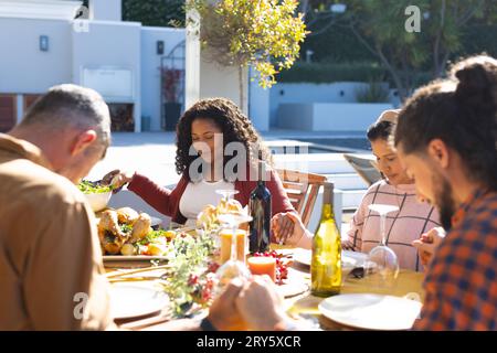 Heureux divers amis masculins et féminins priant avant le repas de célébration de Thanksgiving dans le jardin ensoleillé Banque D'Images